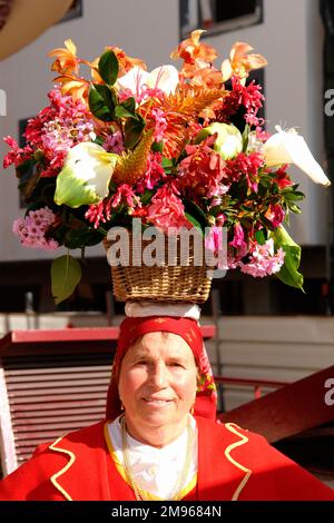 Une femme d'un groupe folklorique du village de Camacha, marchant dans les rues de Funchal, la capitale de Madère, avec un grand panier de fleurs sur sa tête. Banque D'Images