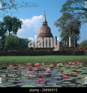 Le temple bouddhiste Wat Chana Songkhram à Old Sukhothai, Thaïlande. Le chedi (tombeau) en forme de cloche est de style cinghalais. Vue sur un étang aux nénuphars aux fleurs roses en fleur. Banque D'Images