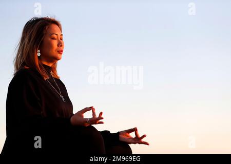 Femme pratiquant la méditation de yoga au bord de la mer avant le coucher du soleil comme concept de silence et de détente. Banque D'Images
