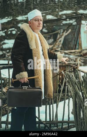 Un médecin vétérinaire avec une valise marche dans un village ranch en hiver dans des vêtements chauds et des bottes en feutre Banque D'Images