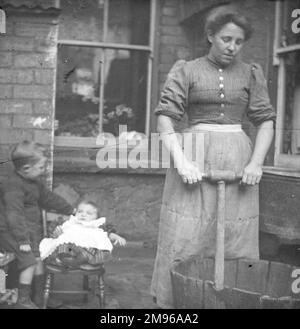 Une femme utilisant une baignoire à roulettes pour faire le lavage hebdomadaire, dans une cour arrière du pays de Galles du Sud, avec deux enfants à gauche. W E Jones a rappelé: 'Les George de venir et de laver une fois par semaine pour ma mère et là vous pouvez voir le vieux tas. Il y a deux de mes frères, Lyndon, le plus jeune, est sur la chaise. Banque D'Images