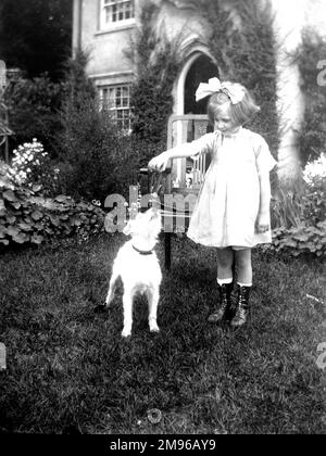 Une petite fille édouardienne dans un jardin avec un petit chien terrier à poil dur. Elle tient quelque chose dans sa main pour que le chien saute et attrape. Banque D'Images