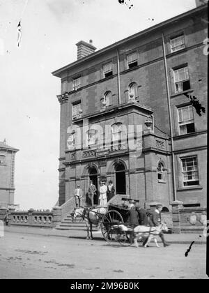 Groupe de personnes habillées sur les marches d'une grande pension Pembrokeshire de cinq étages. Il y a deux chariots dans la chaussée - un grand tiré par un cheval, et un petit tiré par une chèvre. Banque D'Images