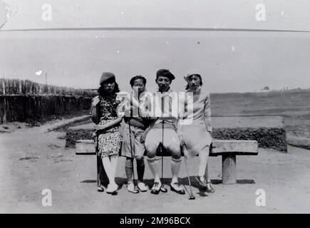 Quatre habitants, deux hommes et deux femmes, assis sur un banc, quelque part en extrême-Orient. Ils portent des vêtements à la mode de style occidental et tiennent des clubs de golf. Il y a un terrain de golf en arrière-plan. Banque D'Images