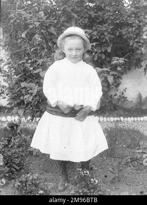 Une petite fille édouardienne dans une robe blanche et une ceinture sombre pose dans un jardin, au centre du pays de Galles. Banque D'Images
