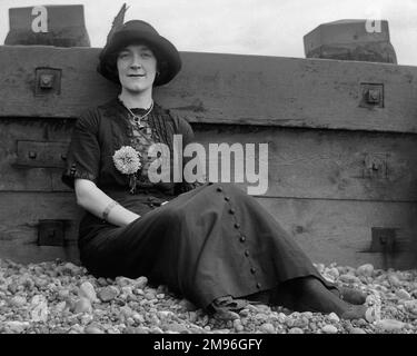 Jeune femme sur une plage de galets, penchée contre un brise-bois. Banque D'Images
