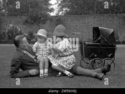 Un homme avec deux petits enfants - un garçon et une fille - et un bébé jouet dans un jardin bien entretenu. Banque D'Images