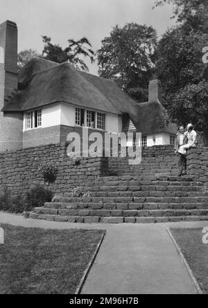 Un couple dans un jardin bien entretenu à l'arrière d'un grand cottage en chaume. Banque D'Images