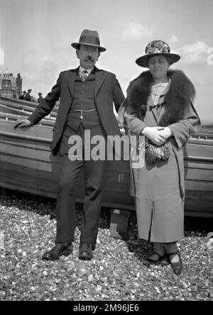 Un couple d'âge moyen debout devant quelques bateaux sur une plage de galets. Banque D'Images