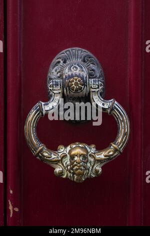 Vue rapprochée d'un knockeur traditionnel de porte en laiton d'époque avec face de l'homme isolé sur une porte en bois rouge foncé, Montpellier, France Banque D'Images