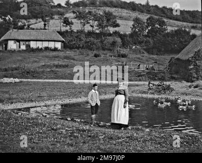 Femme et garçon debout près d'un étang à caillebotis près d'un cottage en chaume. Banque D'Images