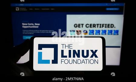 Personne tenant un smartphone avec le logo du consortium de technologie Linux Foundation à l'écran devant le site Web. Mise au point sur l'affichage du téléphone. Banque D'Images