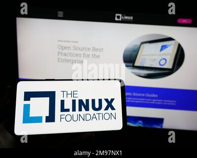 Personne tenant un téléphone portable avec logo du consortium de technologie Linux Foundation à l'écran en face de la page Web. Mise au point sur l'affichage du téléphone. Banque D'Images