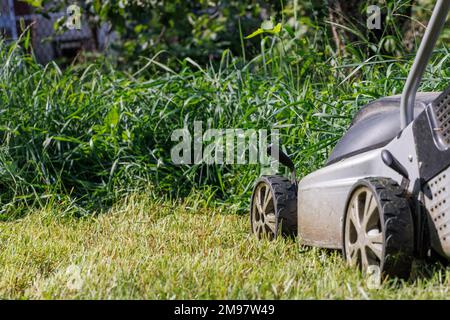 Les roues d'une tondeuse à gazon électrique sur fond d'herbe verte dense et brouillée. Banque D'Images