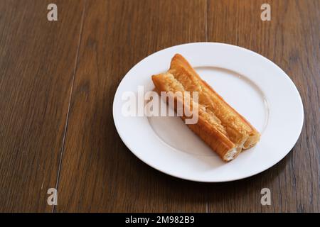 Un morceau de youtiao chinois (bâton de pâte frite) sur une assiette sur une table en bois. En-cas traditionnel pour le petit déjeuner en Chine Banque D'Images