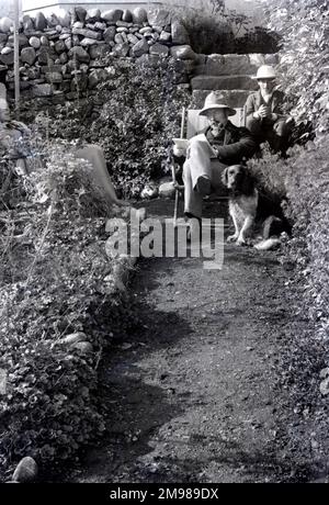 Homme avec un chien et probablement son fils, relaxant et lisant un livre assis dans un transat dans un jardin. Banque D'Images