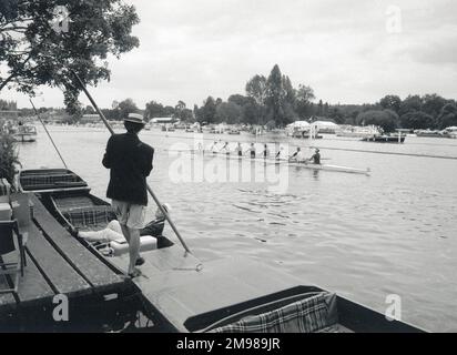 Deux hommes sur un punt, avec des gens qui ravirent au loin à Henley-on-Thames, Oxfordshire, Angleterre. Banque D'Images