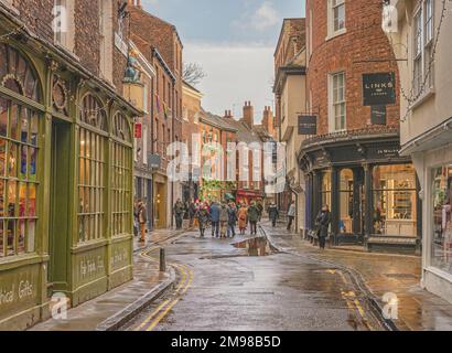 Une ancienne rue de York. Les vieux bâtiments sont de chaque côté et la lumière du soleil tombe sur certains bâtiments. Des boutiques bordent la rue et un ciel nuageux est au-dessus. Banque D'Images