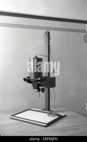 1950s, historique, un agrandisseur de l'époque, sur pied, avec base, plomb et prise, assis sur une table. Cet équipement photographique avait un objectif et était utilisé dans une pièce sombre pour produire des tirages plus grands à partir de négatifs de films d'orginal plus petits. Banque D'Images