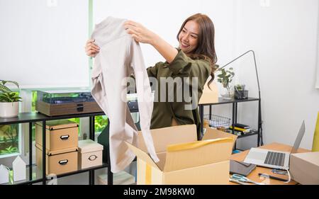 Bonne femme asiatique client ouvrant la boîte après avoir commandé de nouveaux vêtements de mode à la maison Banque D'Images