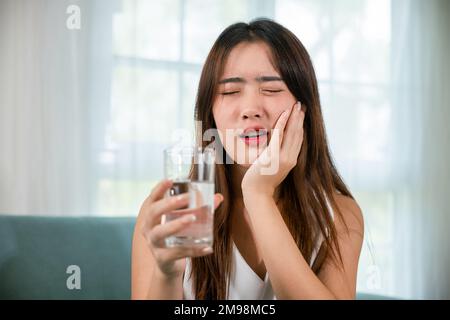 Jeune femme asiatique avec des dents sensibles tenant un verre d'eau froide Banque D'Images