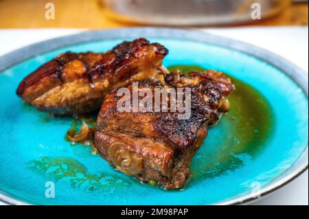 Deux morceaux de poitrine de porc cuite avec une peau croustillante sur la plaque bleue de la table, gros plan. Banque D'Images