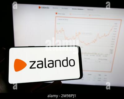 Personne tenant un téléphone mobile avec le logo de la société allemande de commerce électronique Zalando se sur l'écran en face de la page Web d'affaires. Mise au point sur l'affichage du téléphone. Banque D'Images