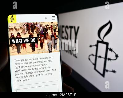 Personne tenant un téléphone portable avec une page web de l'organisation des droits de l'homme Amnesty International à l'écran avec logo. Concentrez-vous sur le centre de l'écran du téléphone. Banque D'Images