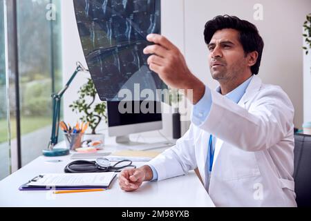 Un médecin portant un manteau blanc assis au bureau regardant un scanner ou un IRM Banque D'Images