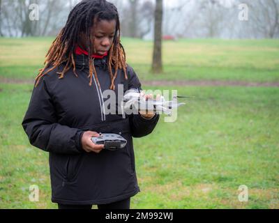 Jeune adolescent afro-américain enjoué portant des vêtements de sport vérifiant voler un drone d'appareil photo dans un parc avant utilisation. Banque D'Images