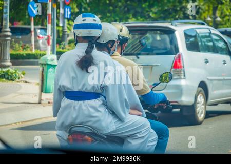 dos d'une fille dans un kimono avec une tresse dans un casque sur un cyclomoteur comme passager Banque D'Images