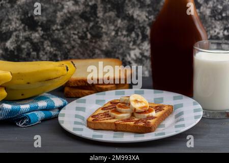 petit déjeuner de pain grillé à la banane et au caramel, accompagné d'un verre de lait sur une table. Banque D'Images