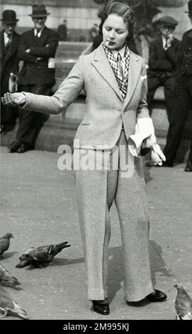 Femme à la mode dans un costume de pantalon nourrissant des pigeons à Trafalgar Square, Londres. Banque D'Images