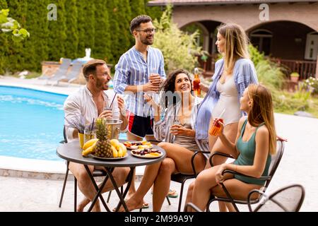 Groupe de jeunes heureux qui applaudissent au cidre près de la piscine dans le jardin Banque D'Images