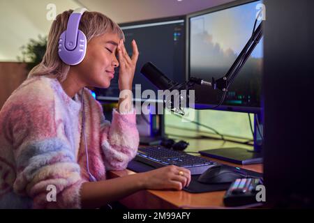 Femme fatiguée qui se fait jouer à la maison assise au bureau avec plusieurs moniteurs Banque D'Images