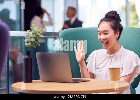 Femme d'affaires ayant un appel vidéo sur ordinateur portable à la table dans la zone de coin salon du bâtiment de bureau Banque D'Images