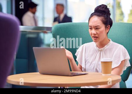 Femme d'affaires ayant un appel vidéo sur ordinateur portable à la table dans la zone de coin salon du bâtiment de bureau Banque D'Images