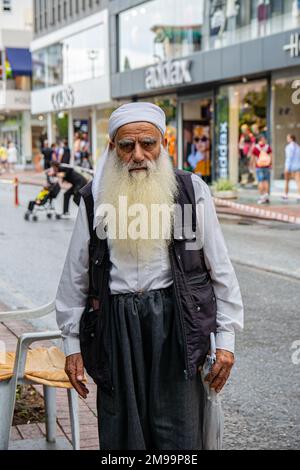 Alanya, Turquie, 16.10.2022: Un vieil homme avec une longue barbe grise est habillé de style arabe dans la rue d'une ville turque. Un homme coloré regarde le Banque D'Images