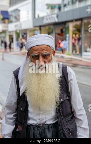 Alanya, Turquie, 16.10.2022: Un vieil homme avec une longue barbe grise est habillé de style arabe dans la rue d'une ville turque. Un homme coloré regarde le Banque D'Images