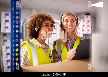 Deux travailleuses portant des micro-casques dans l'entrepôt de distribution logistique utilisant une tablette numérique Banque D'Images