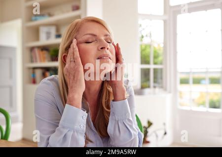 Femme ménopausique mature à la maison souffrant de maux de tête Banque D'Images