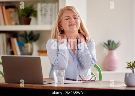 Menopausal mature femme souffrant de douleur de cou travailler sur ordinateur portable à la maison Banque D'Images