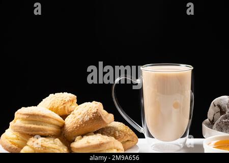 Thé avec du lait dans une tasse en verre avec un double fond et des gâteaux sur fond noir, placer pour le texte Banque D'Images