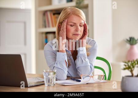 Femme adulte ménopausique travaillant sur un ordinateur portable à la maison souffrant de maux de tête Banque D'Images