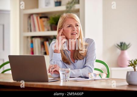 Femme mature travaillant sur un ordinateur portable assis à la table à la maison Banque D'Images