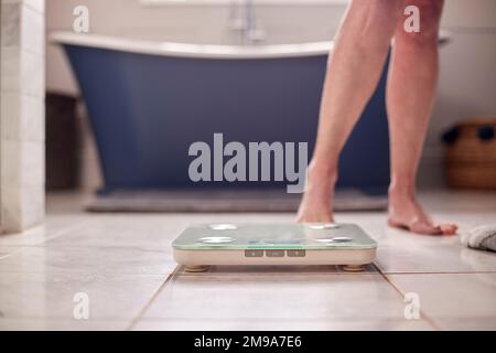 Gros plan de la femme âgée ménopausique concernée par le gain de poids debout sur des balances dans la salle de bains Banque D'Images