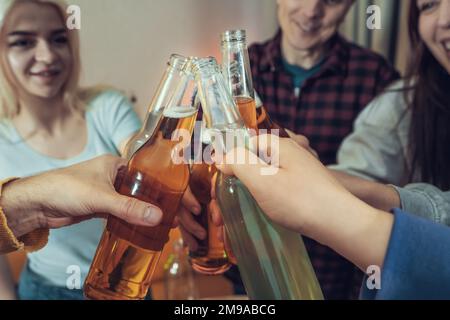 Des amis qui se trinchent des bouteilles de bière à la fête à la maison, gros plan sur les mains. Célébration et fêtes concept. Banque D'Images