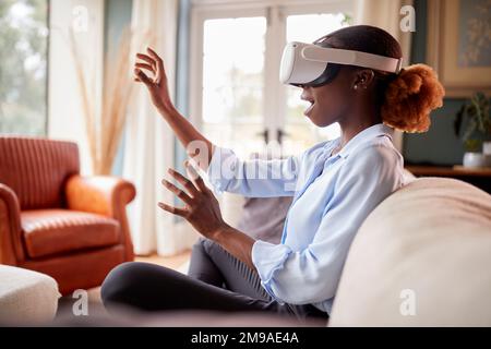 Femme se détendant sur un canapé à la maison, portant un casque VR et interagissant avec la technologie AR Banque D'Images