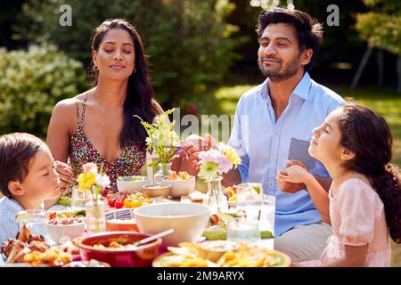 Famille religieuse disant prières ou grâce avant de manger un repas en plein air dans le jardin Banque D'Images