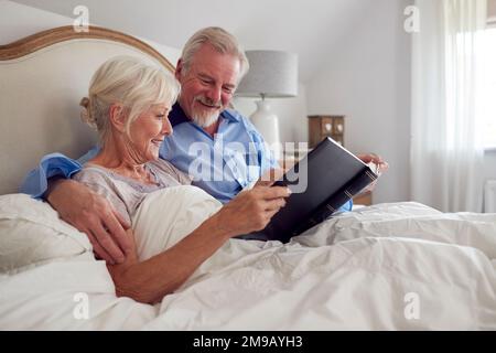 Couple senior retraité au lit à la maison regardant ensemble l'album photo Banque D'Images